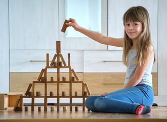 Happy child girl playing game stacking wooden toy blocks in high pile structure. Hand movement control and building computational skills concept