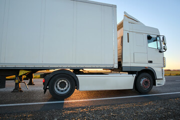 Semi-truck with cargo trailer driving on highway hauling goods in evening. Delivery transportation and logistics concept