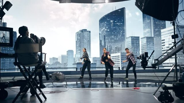 Music Clip Studio Set: Shooting Hip Hop Video Dance Scene with Three Professionals Dancers Performing on Stage with Big Led Screen with Modern City Background. Director and Cameraman in Backstage.