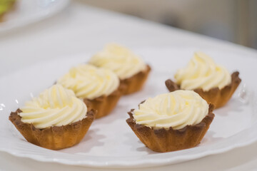 Assortment of delicious fresh shortcrust tart cakes with cream on white plate for sale at restaurant, cafe, bakery. Dessert, culinary, sweet food and confectionery concept