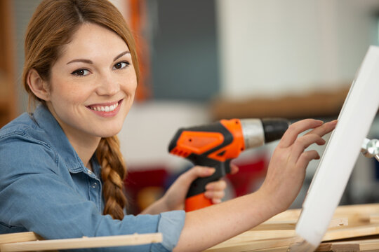 female worker using orange drill on wooden pieces