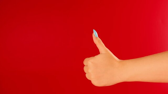 Woman's hand showing thumb up on red background with space for text. Unrecognizable person showing gesture of like.