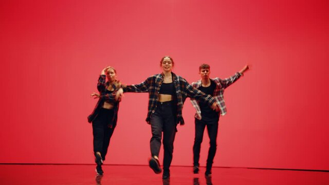 Diverse Group of Three Professional Dancers Performing a Hip Hop Dance Routine in Front of a Big Digital Led Wall Screen with Changing Warm Color Background (Red, Pink, Orange) in Studio Environment.