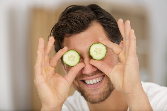 playful man holding slices of cucumber over his eyes
