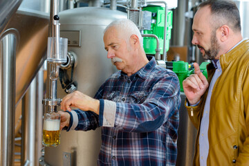 mature men in brewery dispensing beer to sample
