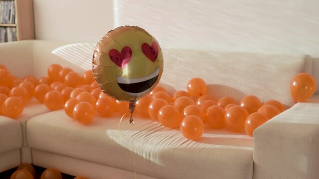 Smiley balloon filled with helium hovering in an apartment in front of a sofa after a party