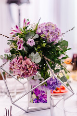 Wedding decor. Festive table decorated with composition of violet, purple, pink flowers and greenery in the banquet hall.