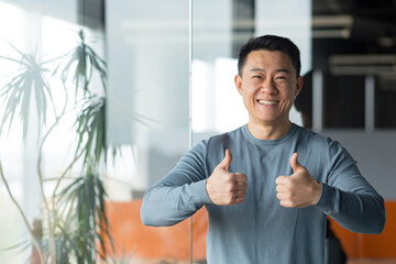 portrait of asian businessman freelancer in modern office, man with arms crossed happy and smiling looking at camera