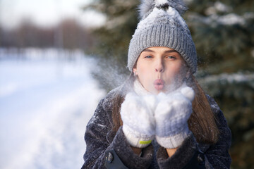 Portrait of beautiful attractive happy girl, young positive pretty woman is blowing snow from her...