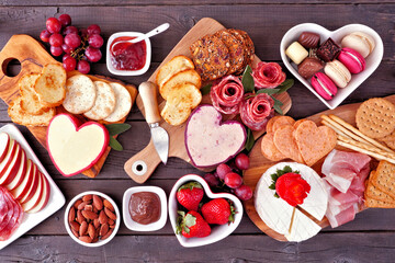 Valentine's Day theme charcuterie table scene against a dark wood background. Assorted cheese,...