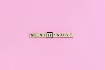 Menopause word and pause sign on wooden blocks with lettering on pink background. Minimal concept...