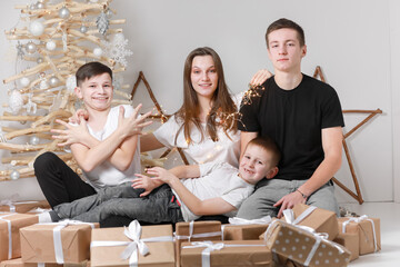 Holidays Concept. cute teenagers are sitting by the wooden decorations Christmas tree and many gift...
