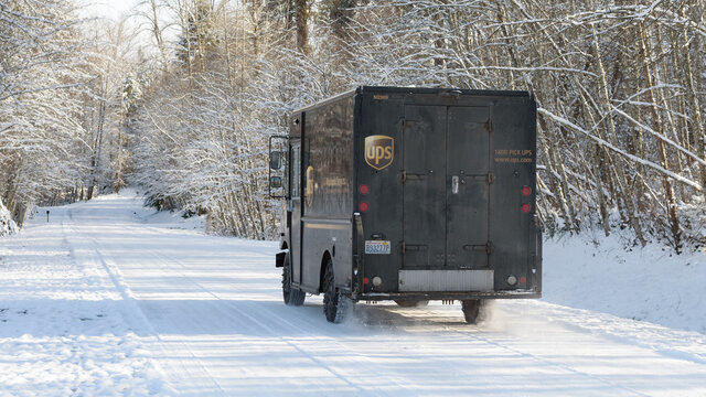 Carnation, WA, USA - December 29, 2021; A UPS delivery truck drives on a snow covered road with snow on the winter trees