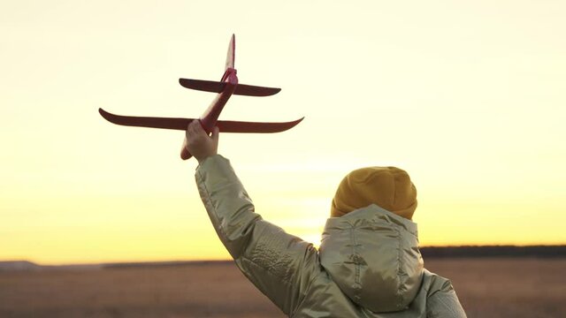 little child runs at sunset with toy plane in his hands, happy family life, childhood dream of flying, running kid fantasizes about pilot's flight, cheerful baby runner in nature travels on weekends