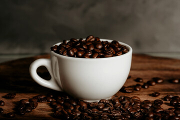 White cup with roasted coffee beans on dark background.