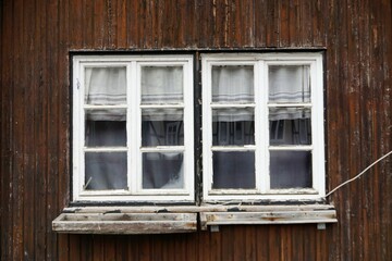 Zwei weiße alte Holzrahmenfenster mit weißen Gardinen in alter Fachwerkscheune auf dem Land bei...