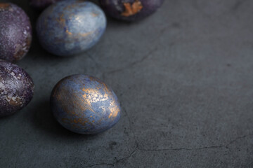 Easter card with a copy of the place for the text. Purple, blue and golden eggs on a dark background. The trend of 2022 purple shade is very peri. Natural dye karkade tea. Top view.