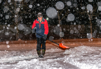 Elderly man with a shovel in his hands clears the street after a heavy snowfall. Man at seasonal work