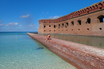 Female in red bikini and Panama hat sitting on rock wall at Dry Tortugas National Park