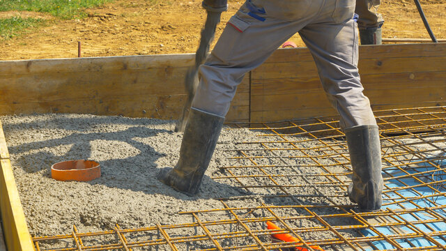 CLOSE UP: Contractors pour rough wet concrete over a reinforced steel net.