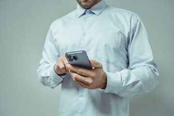 Close-up of a person in a light blue shirt using a smartphone. The individual's hands are gently holding the device, which features multiple camera lenses on the rear.