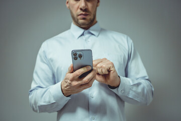 Close-up of a person in a light blue shirt using a smartphone. The individual's hands are gently holding the device, which features multiple camera lenses on the rear.