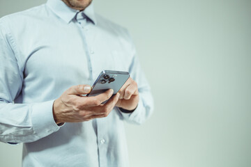 Close-up of a person in a light blue shirt using a smartphone. The focus is on the hands holding the device.