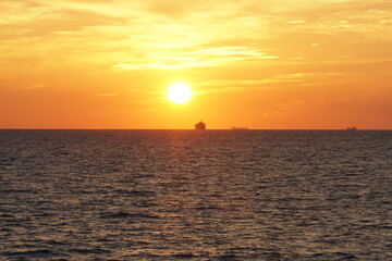 Silhouette of merchant ships on the horizon of calm Pacific ocean during sunset in autumn season....