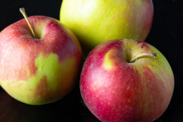 Three red-yellow ripe apples on black background close-up