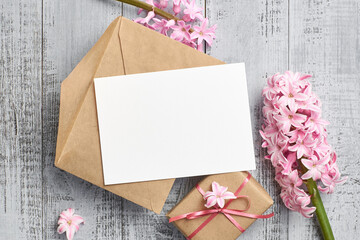 Greeting or invitation card mockup with gift box, envelope and hyacinth flowers on wooden background