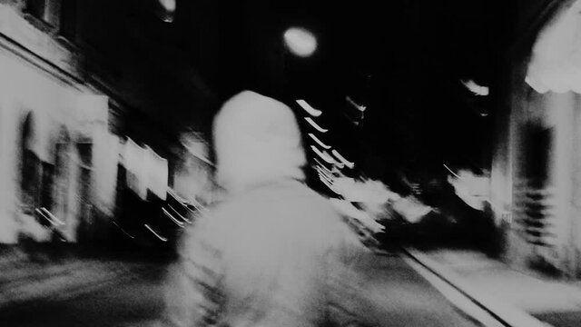 One person walking through the city. Night motion hyper lapse. Urban lights movement. Following a man down the street. Experimental video with lens blur and camera noise.