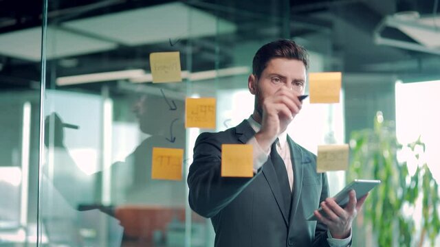 business man in modern office uses post sticky notes digital tablet to share an idea. brainstorming, serious thinking male solving strategy. Use glass note wall Board and Sticky Papers. new startup