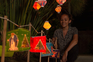 casually dressed Hispanic young woman smiling, under a plant decorated with colorful paper lanterns