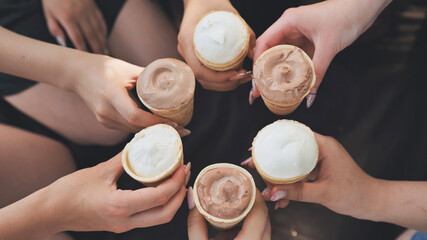 Girls friends join hands with ice cream in waffle cups in a circle.