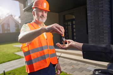 Male construction worker passing keys to house