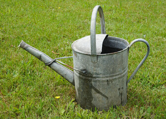 Old vintage style watering can on grass lawn. Rustic tin watering can for gardening use. 