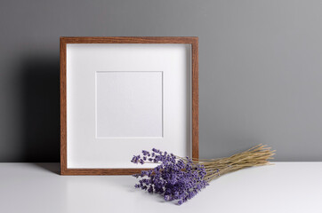 Square wooden frame mockup for artwork, photo, print and painting presentation with dry lavender flowers over grey wall.