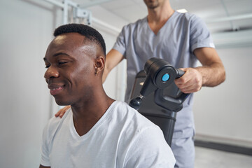 Pleased patient having his neck massaged with percussion gun