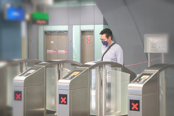 Asian man with face mask on going through subway or metro ticket gates. Masked transit concept.
