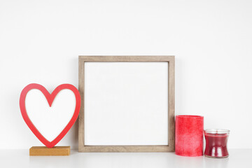 Fototapeta Mock up square wood frame with Valentines Day blank heart sign and candles. White shelf against a white wall. Copy space. obraz