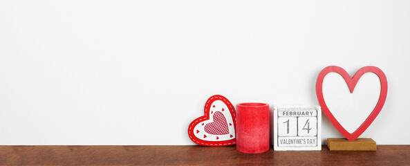 Valentines Day heart decor, candle and rustic wood calendar. Wood shelf against a white wall banner. Copy space.