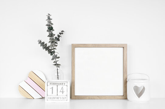 Mock up square wood frame with Valentines Day heart decor and calendar. White shelf against a white wall. Copy space.