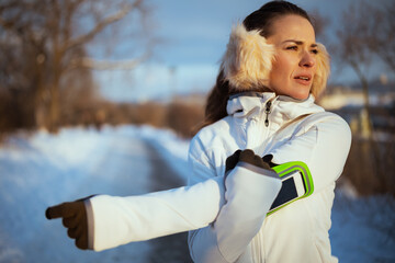 active woman in white jacket with ear warmer stretching