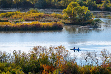 Two people rowing their canoe on the calm waters of a lake or river with the brilliant autumn colors of their surroundings glowing in the sun