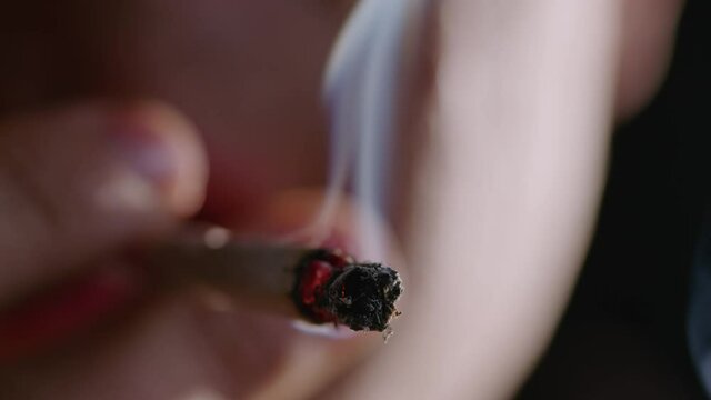 Close-up shot of a burning marijuana joint and blowing smoke into the camera.