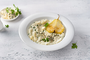 Delicious homemade pear and blue cheese risotto with parsley in white bowl on gray bluebackground