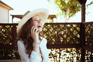 smiling housewife in white shirt speaking on smartphone