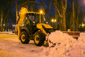 cleaning snow in the park in winter with a tractor in the evening