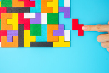 Hand connecting colorful wood puzzle pieces on blue background, geometric shape block. Concepts of...