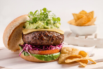 Gourmet burger prepared with avocado, sprouts, cheese, beef, purple cabbage, tomato, lettuce head and white bread, accompanied by Mexican nachos.